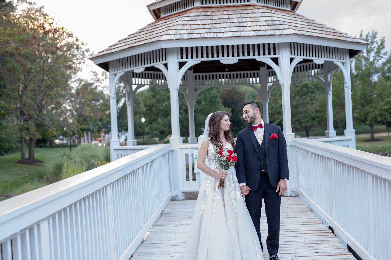 Bride and groom holding hands beneath a white outdoor gazebo